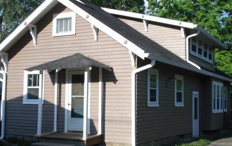 Small brown house with white trim and a covered front porch in a sunny yard