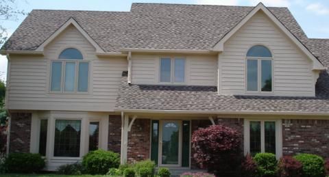 Suburban two-story house with beige siding, brick accents, and manicured shrubs in front