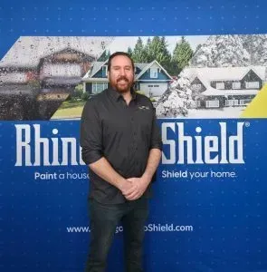 Man standing in front of a Rhino Shield promotional backdrop with houses and logo.