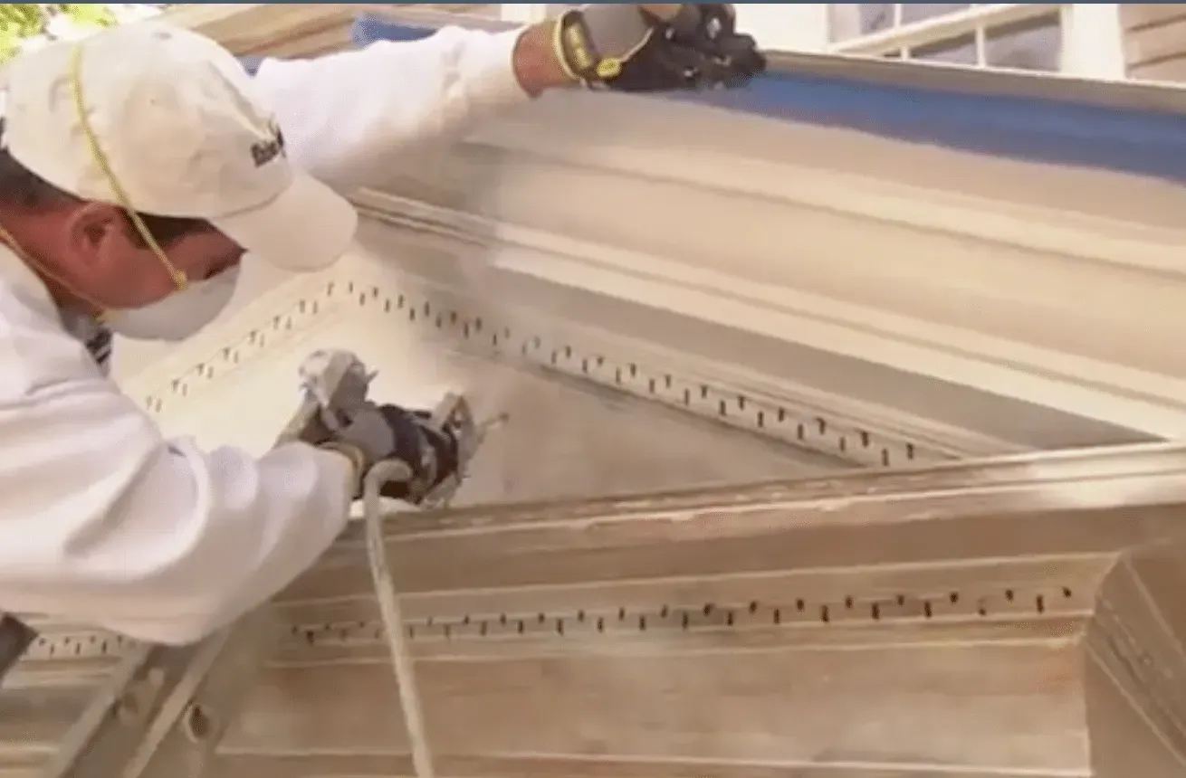 Worker using a pressure washer to clean ornate white moldings indoors