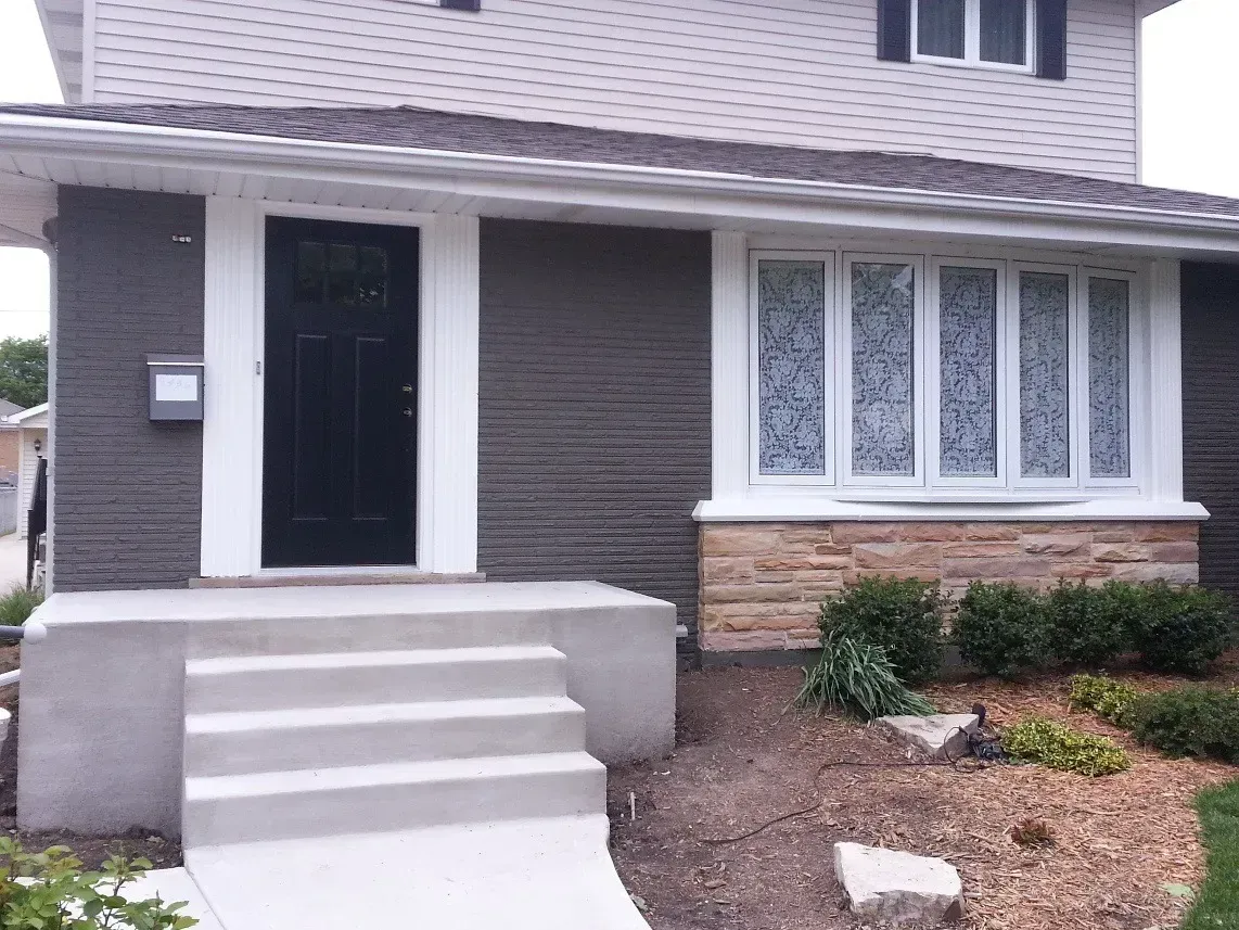 Front entrance of a house with concrete steps, dark front door, and brick and white siding facade.