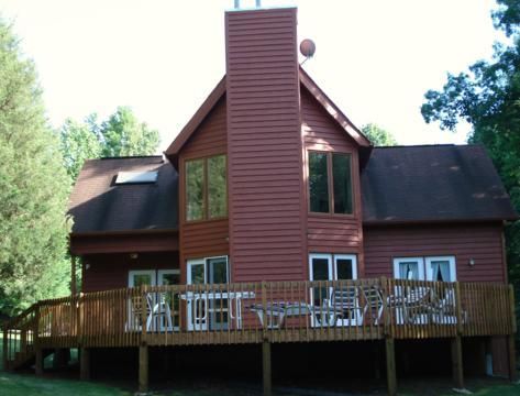 Red wooden house with a tall central chimney and wraparound deck in a wooded setting
