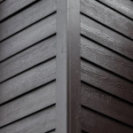 Close-up of dark gray wooden siding meeting at an exterior corner with diagonal slats.