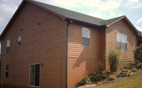 Brown two-story house with tan trim on a sloped hillside under a partly cloudy sky