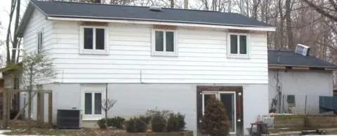Two-story white house with black roof and front door, set behind a small yard