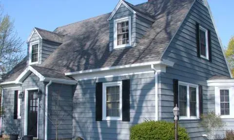 Gray clapboard house with white trim and steep roof, shown from the front in daylight