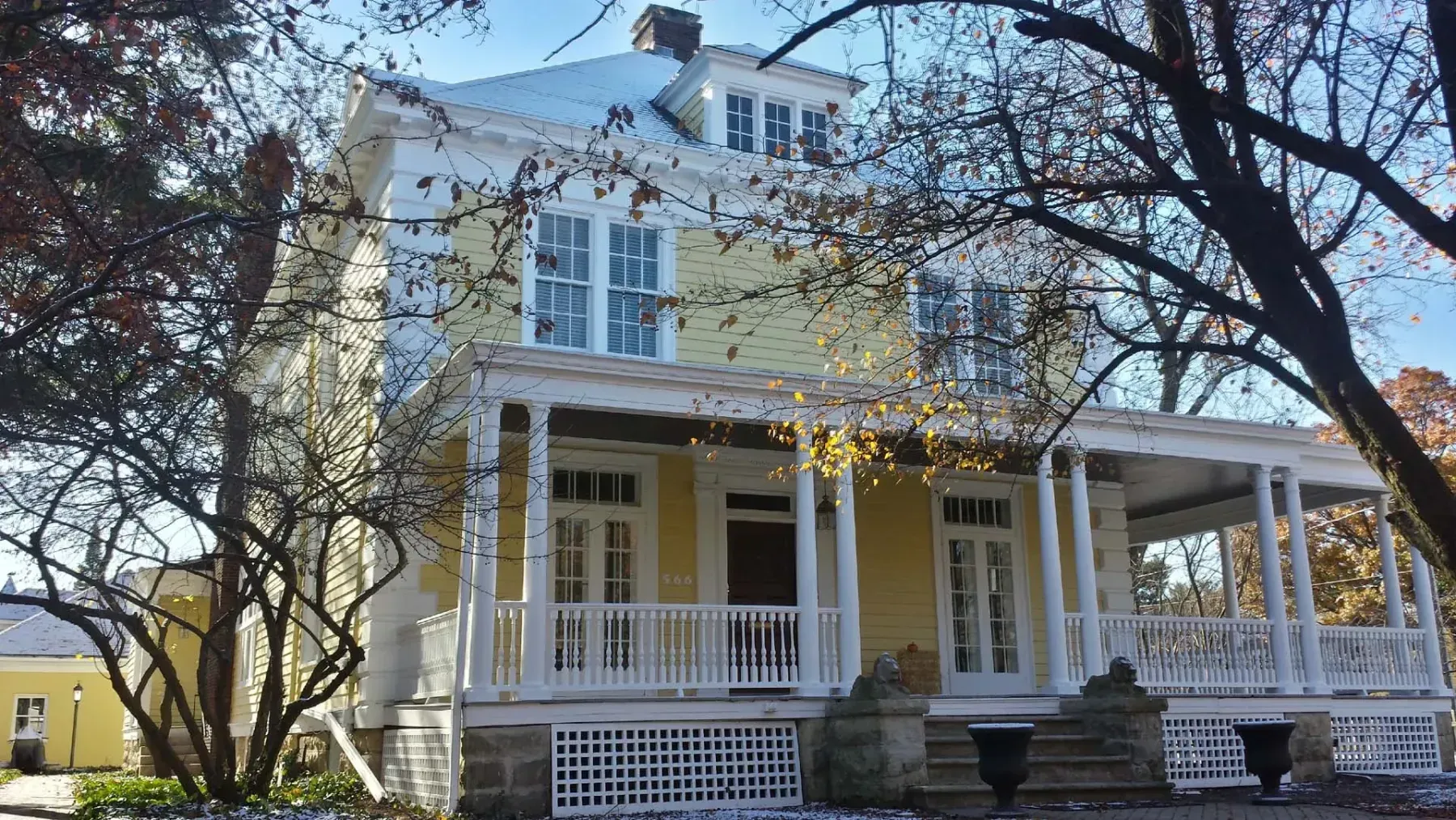 Large white Victorian house with a wraparound porch and trees in the yard
