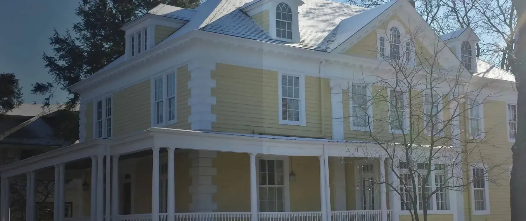 Yellow two-story house with white trim, front porch, and trees in the yard