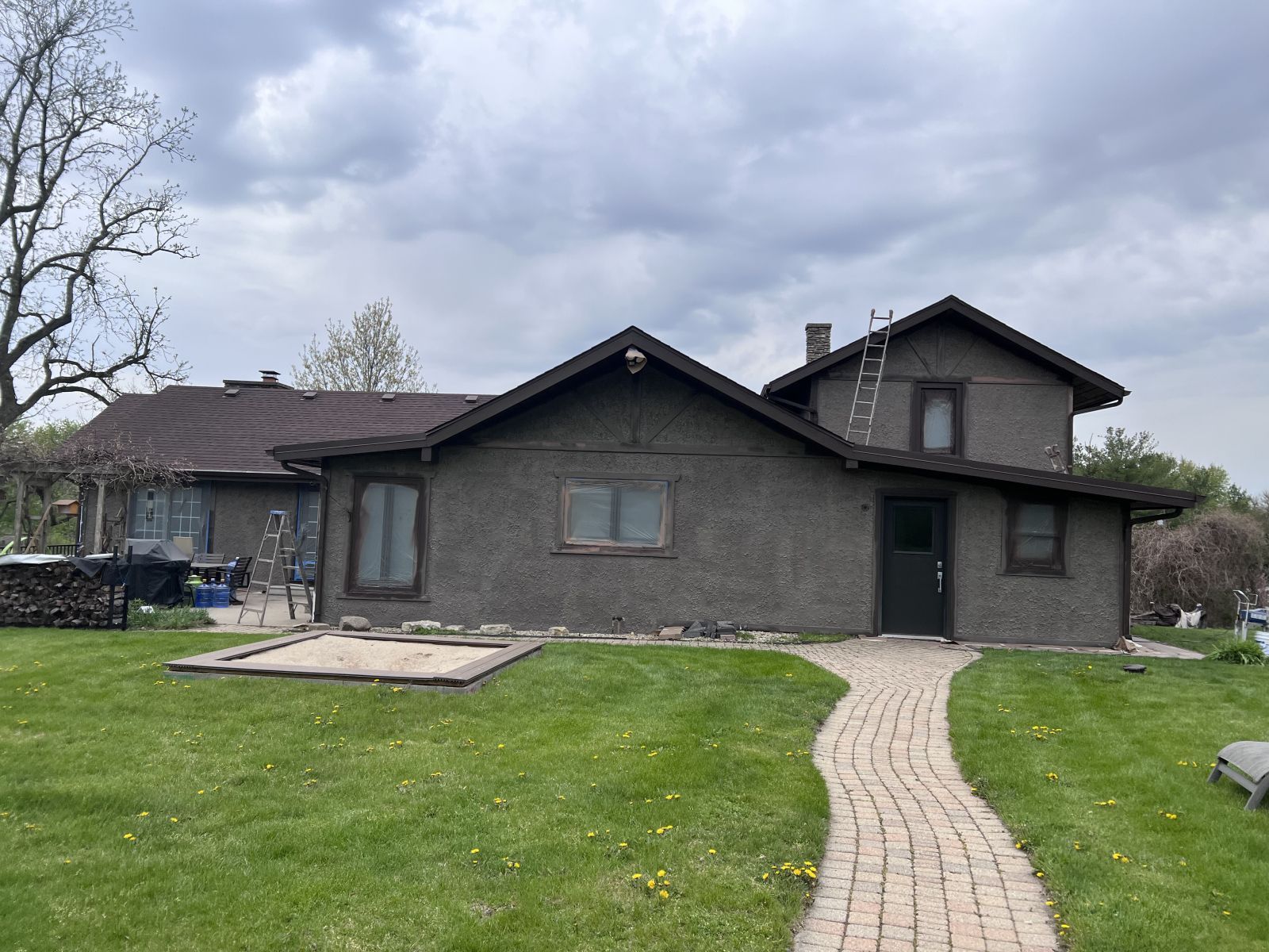 Gray house with a curved brick walkway and green lawn under a cloudy sky