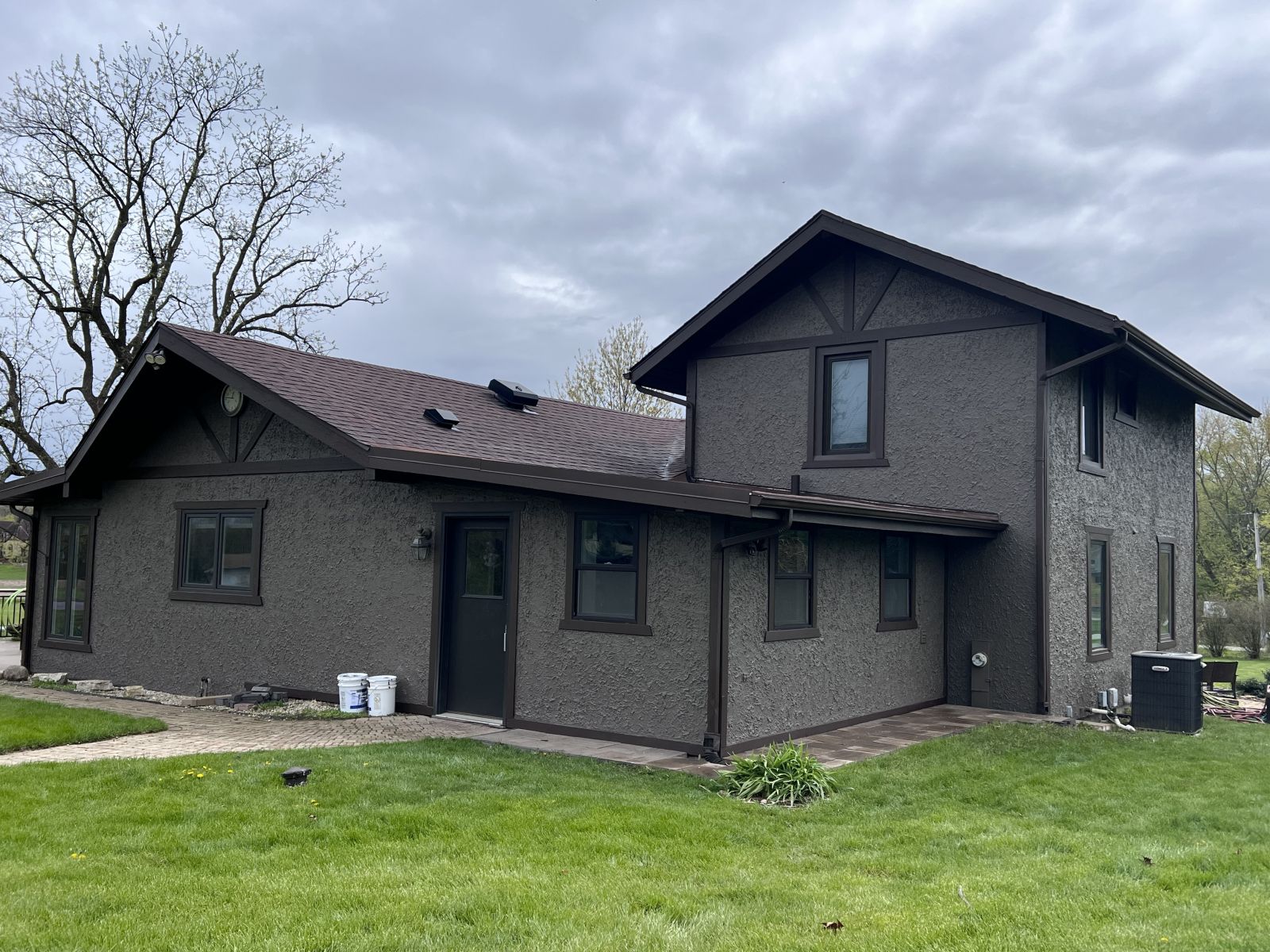 Dark gray two-story house with a sloped roof and lawn, under an overcast sky.