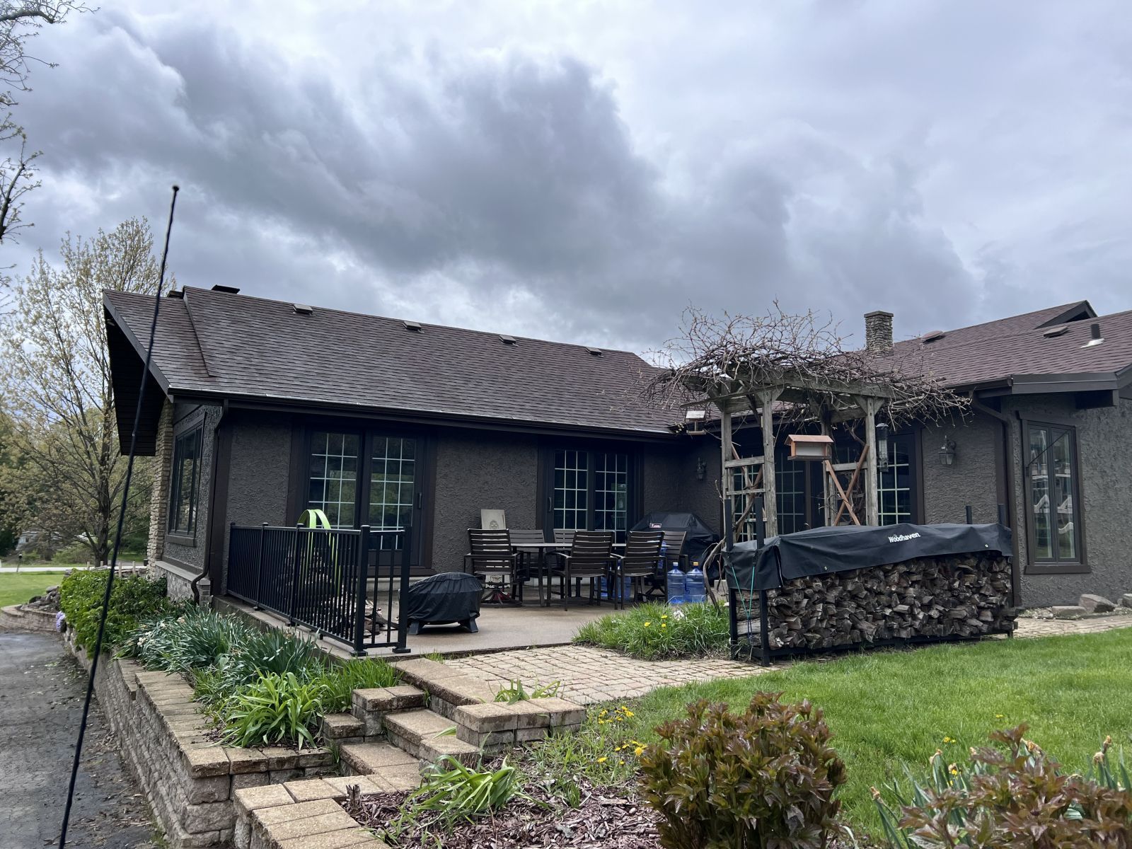 Dark house with curved roof and patio, viewed from a grassy yard under cloudy skies.