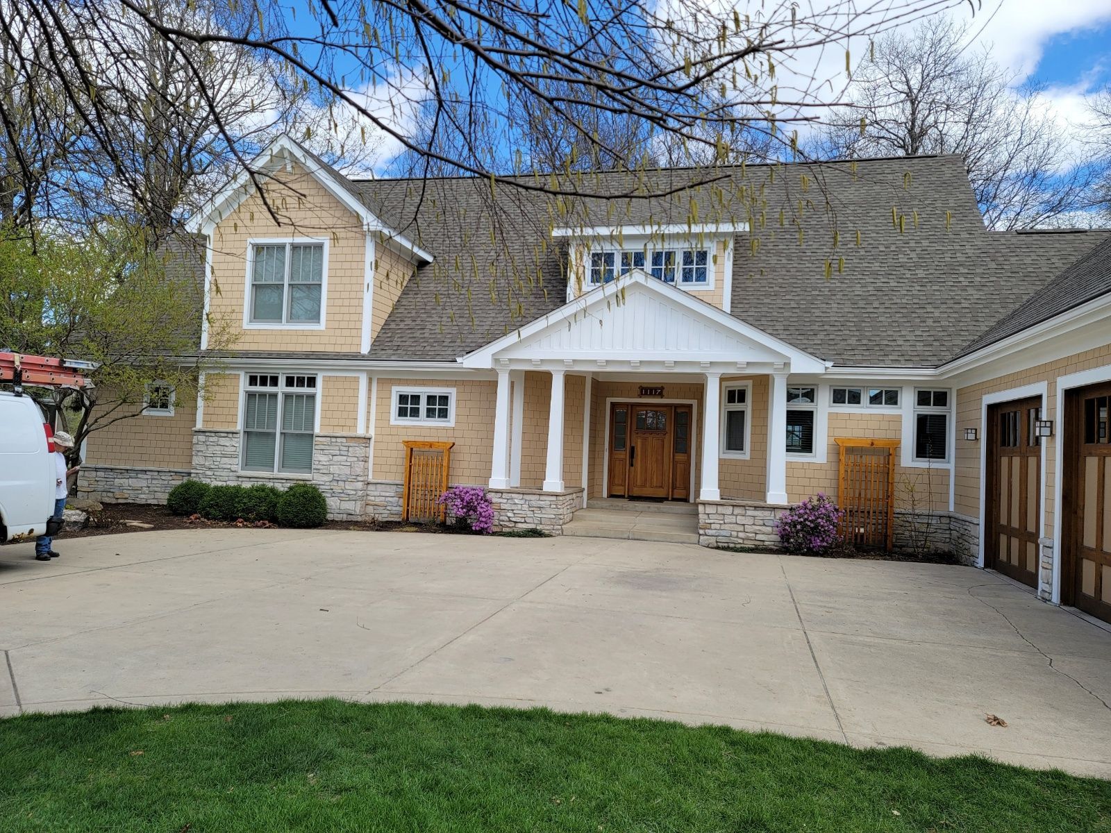 Brick house with large driveway, wooden front door, and attached garage under a cloudy sky