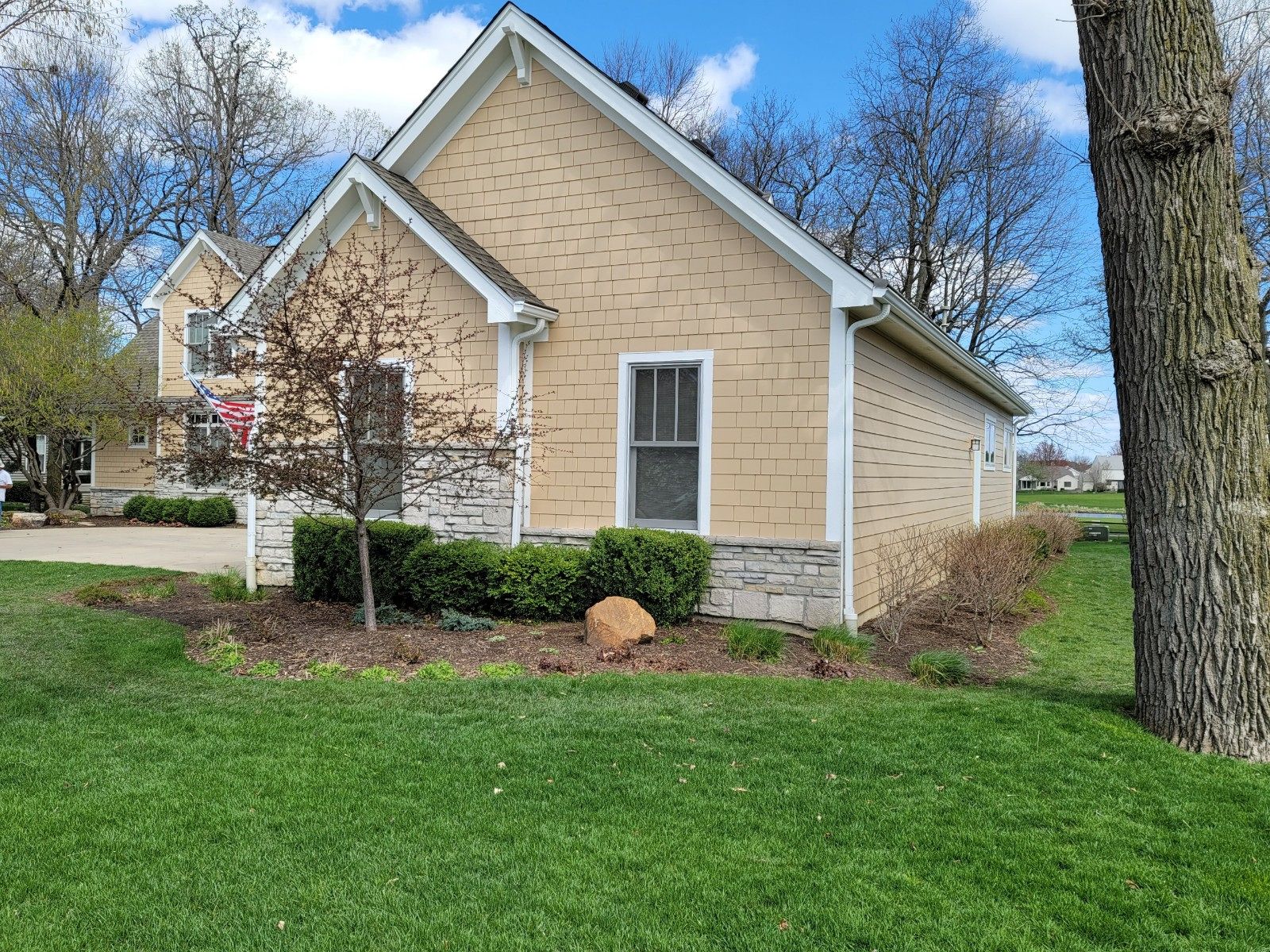 Tan house with stone trim and white trim in a grassy yard under a blue sky