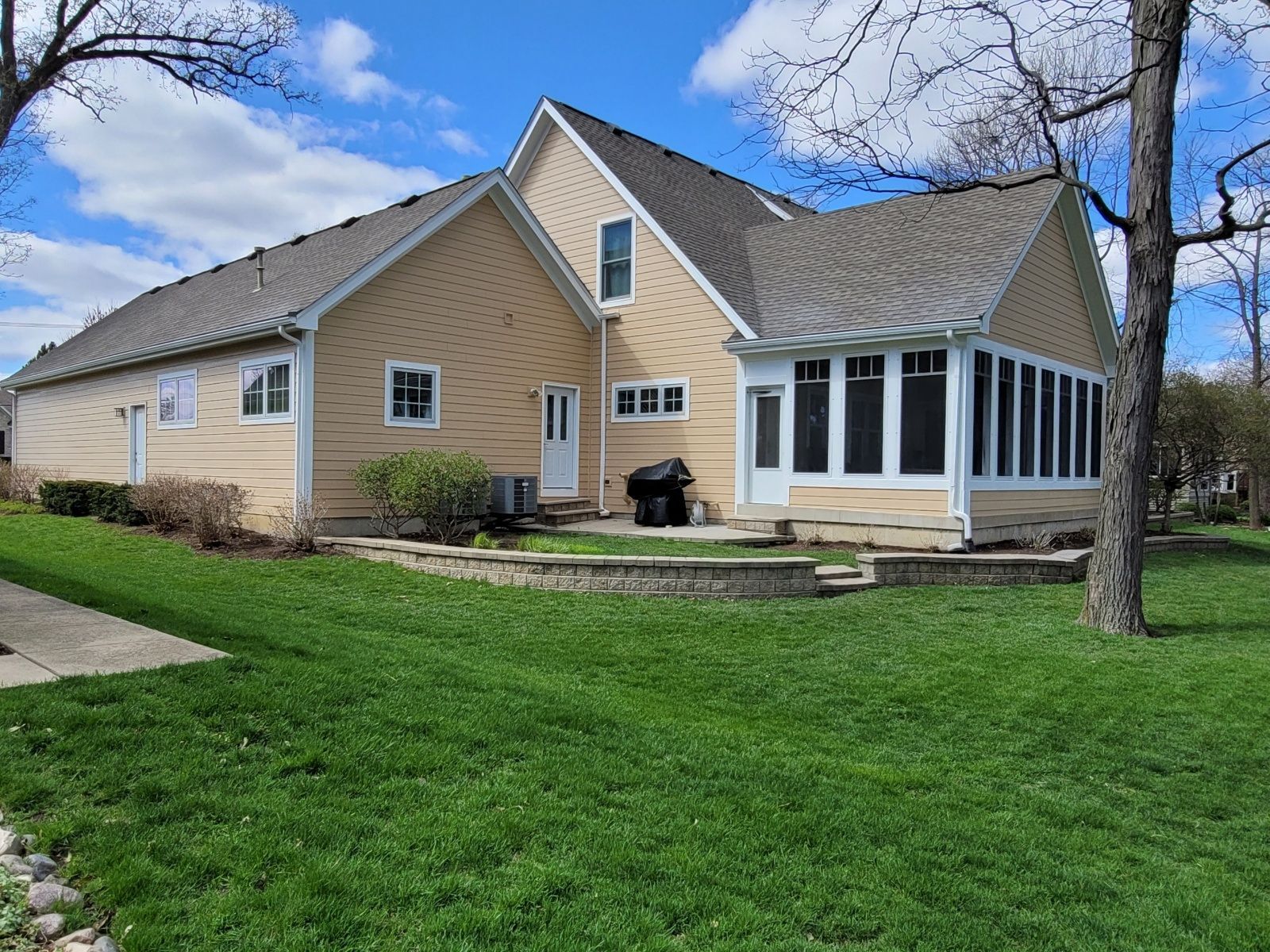 Tan house with white sunroom and large green lawn under a partly cloudy sky