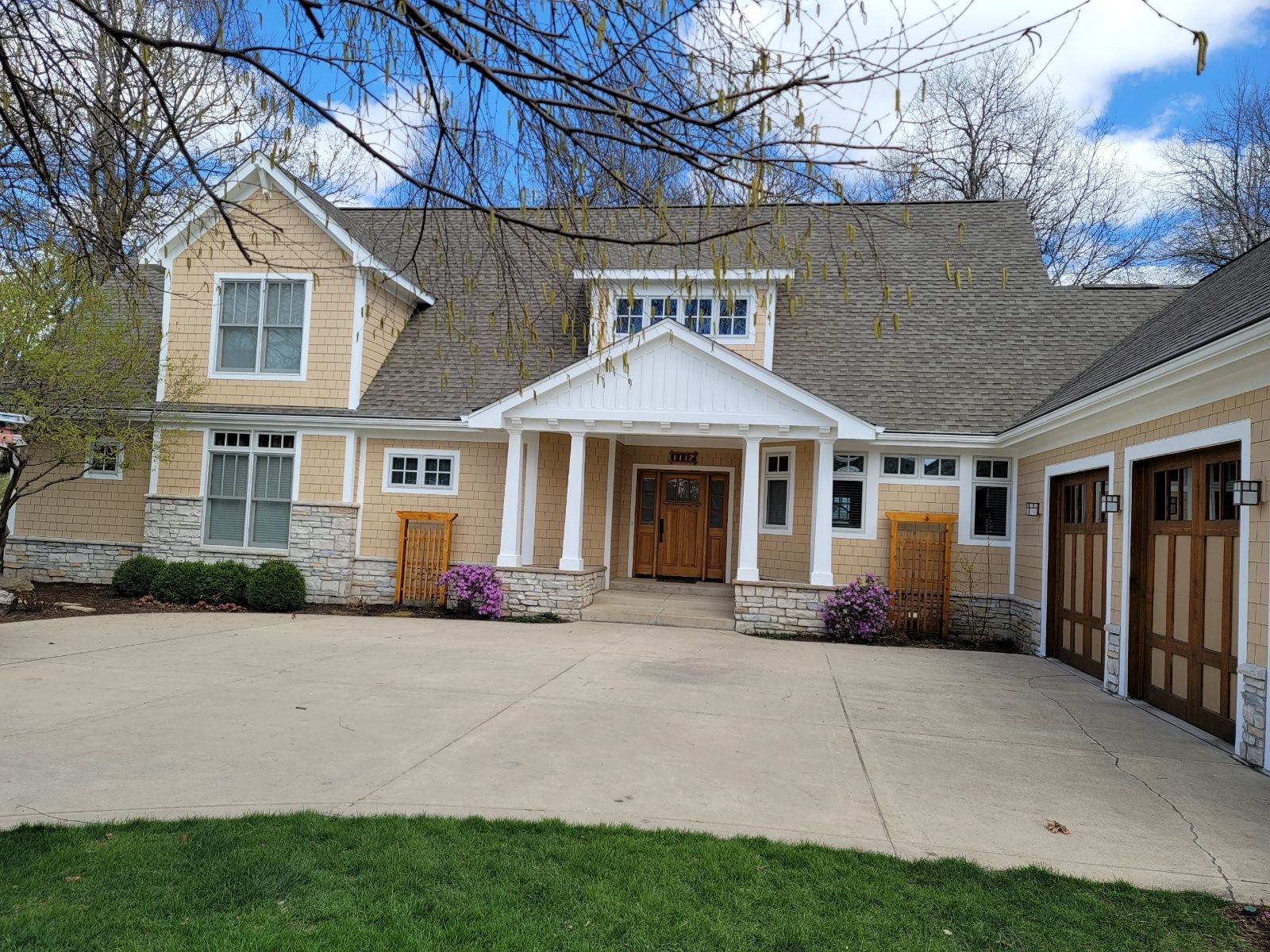 Large beige house with a double garage, white columns, and a wide concrete driveway under a blue sky
