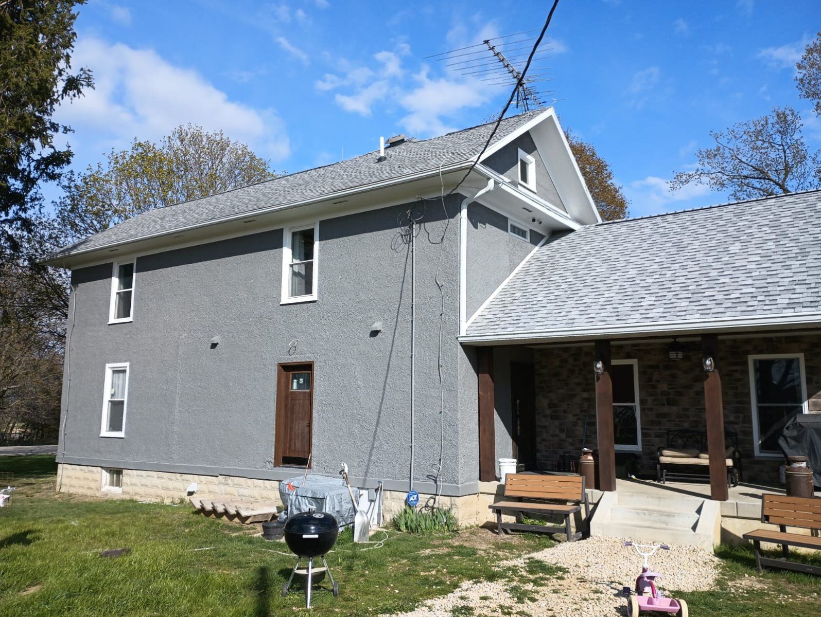 Gray two-story house with white roof, brick porch, and lawn under a blue sky