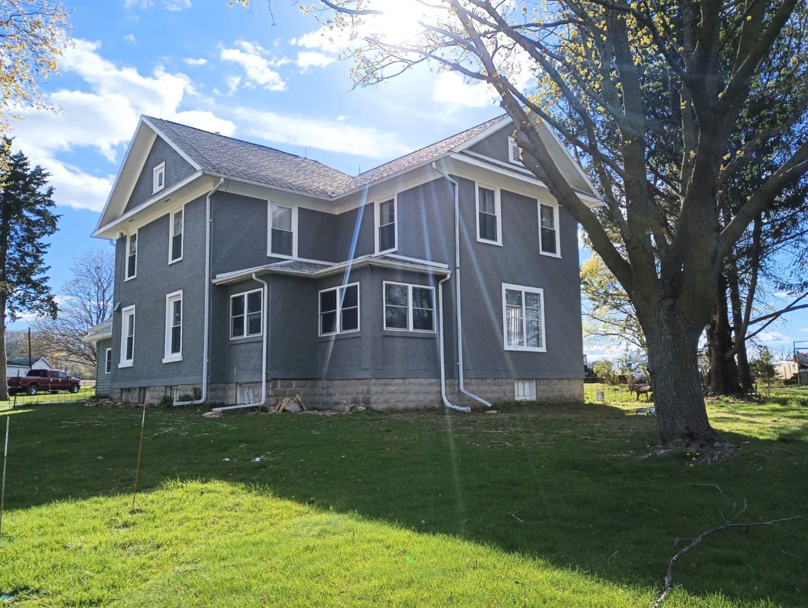 Gray two-story house with white trim and a large tree on a sunny grassy lot