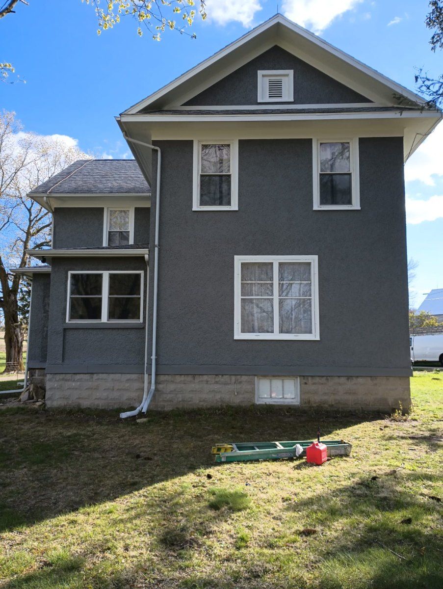 Gray two-story house with white trim and dormer window, viewed from the backyard on a sunny day