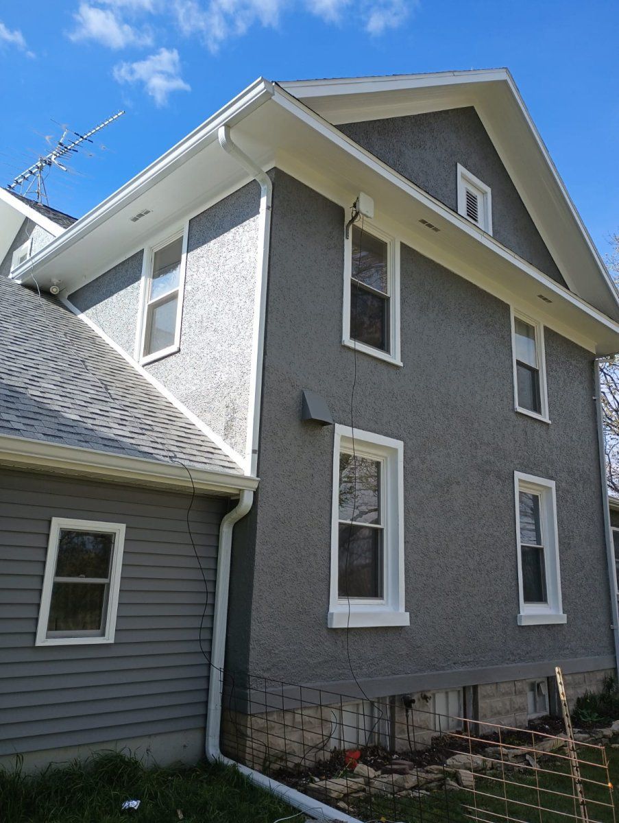 Gray two-story house with white trim and steep roof, viewed from the side against a blue sky