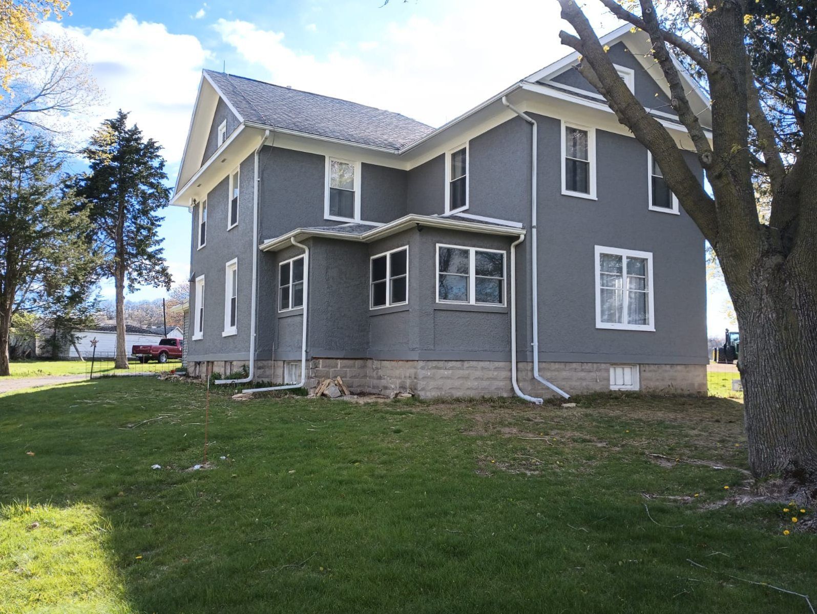 Gray two-story house with white trim, a porch, and a large tree in the yard.