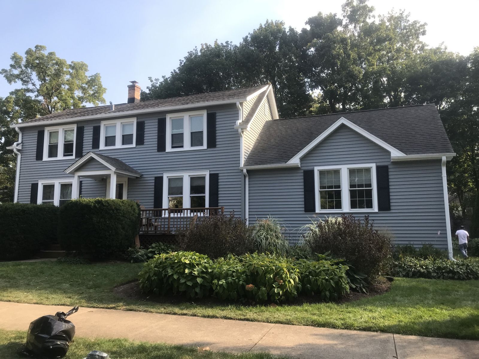 Gray two-story house with white trim, dark shutters, and a landscaped front yard on a sunny day