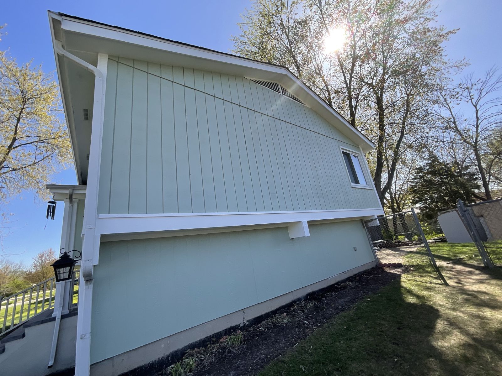 Side view of a light blue house with white trim and a sloped roof in a sunny yard.