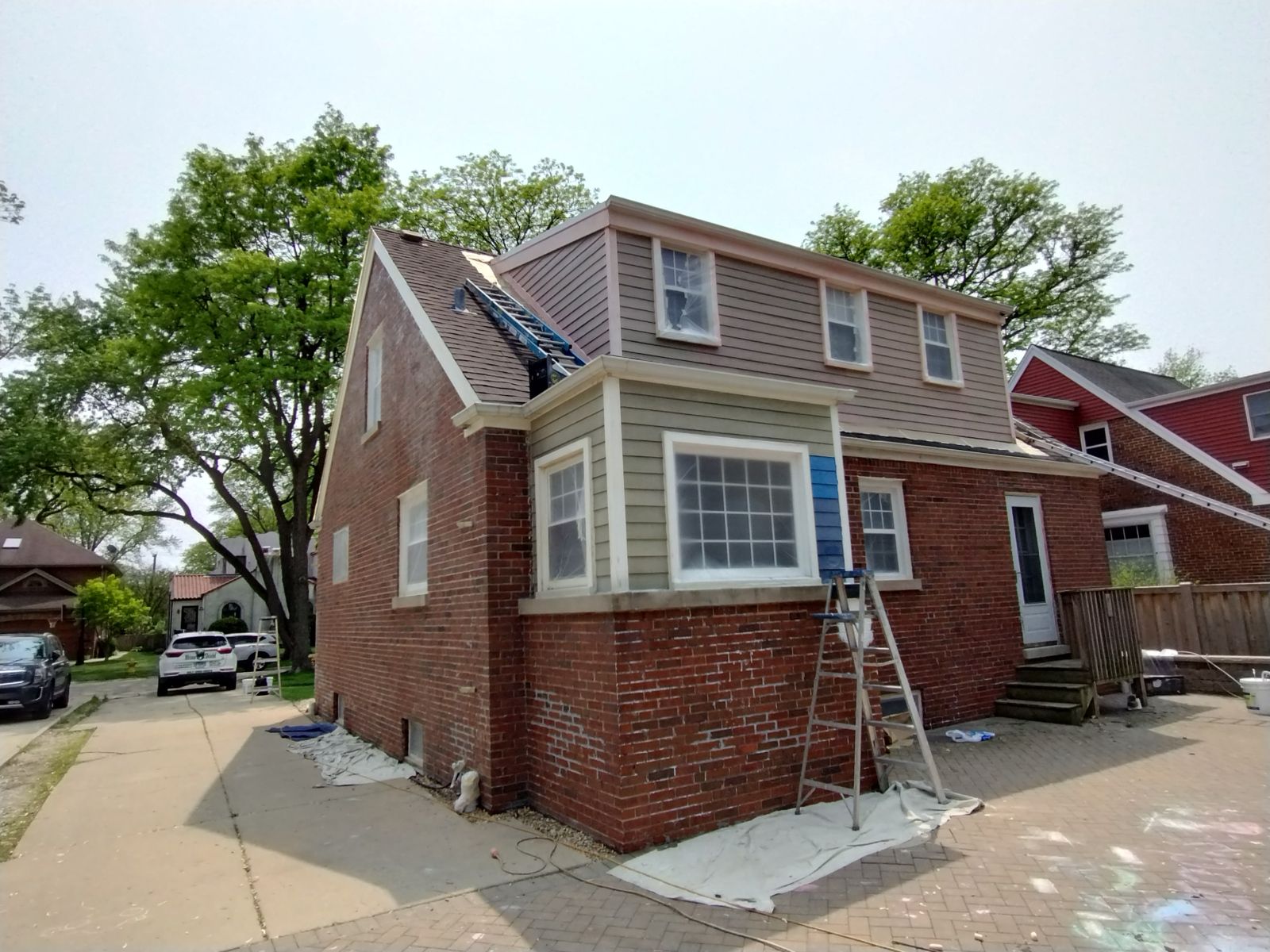Brick house exterior with ladder propped against a window on a sunny residential street