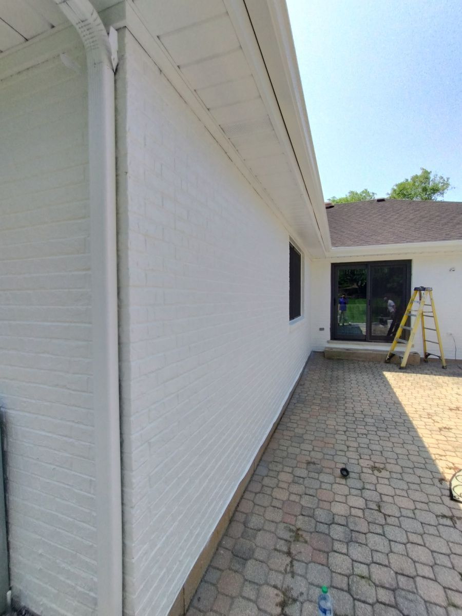 White brick house exterior with a narrow walkway, patio doors, and a ladder near the entrance