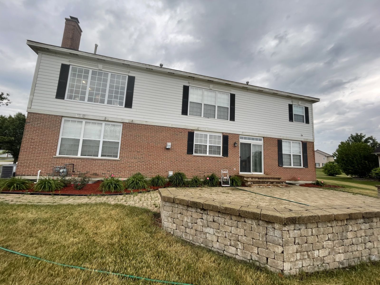 Two-story brick-and-white house with a raised front patio and cloudy sky overhead