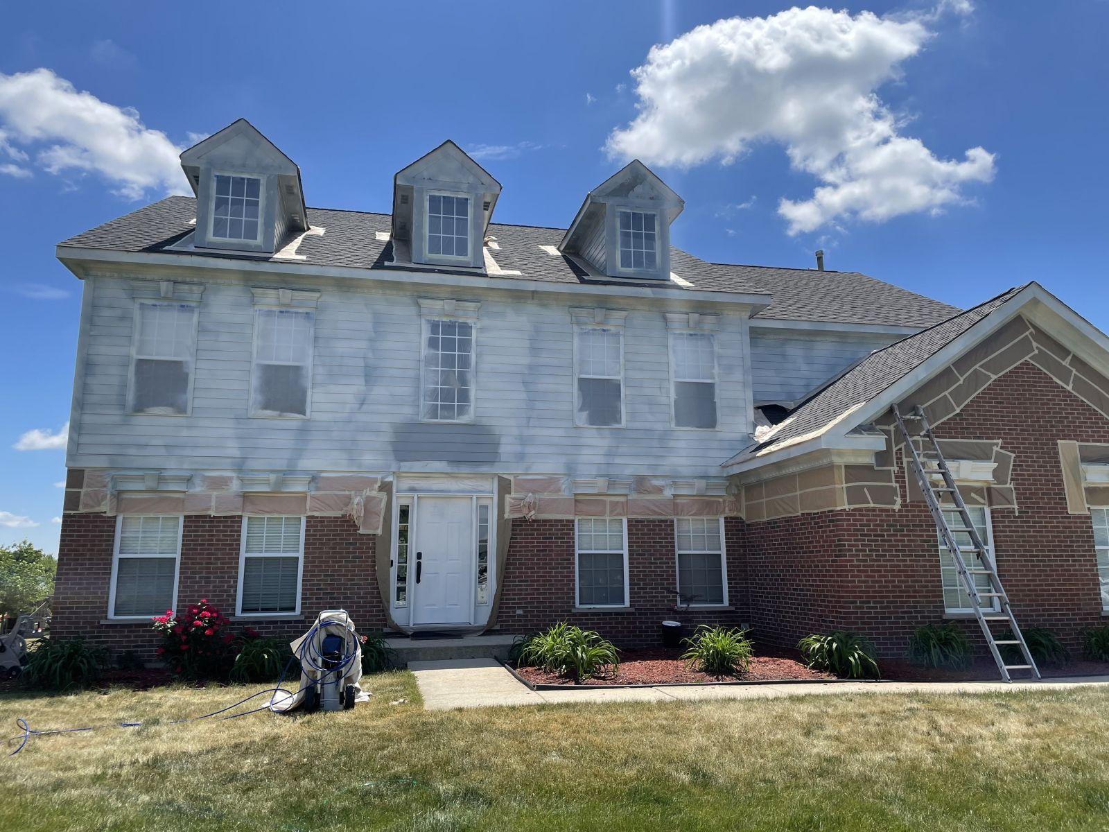 Partially renovated brick townhouse with white sheathing, blue sky, and a ladder on the right side
