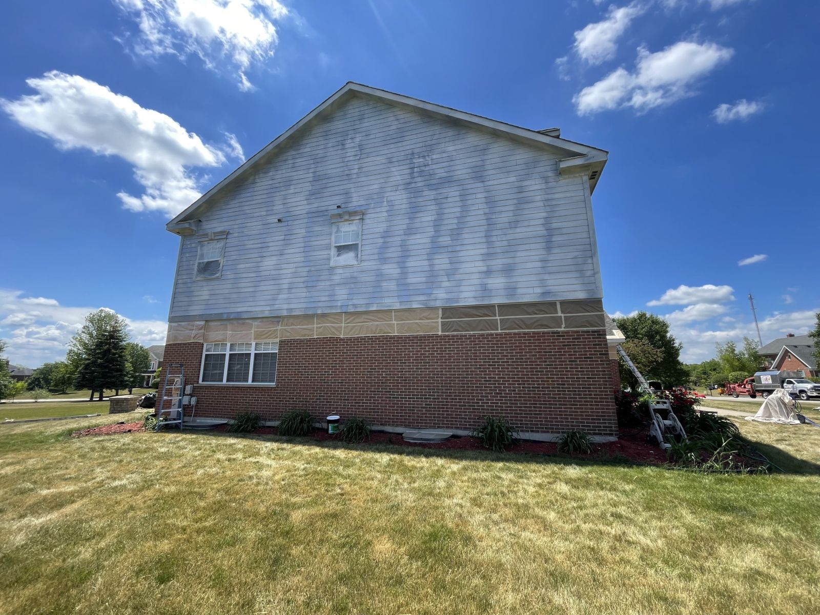 Side view of a house with white siding and brick lower walls under a blue sky