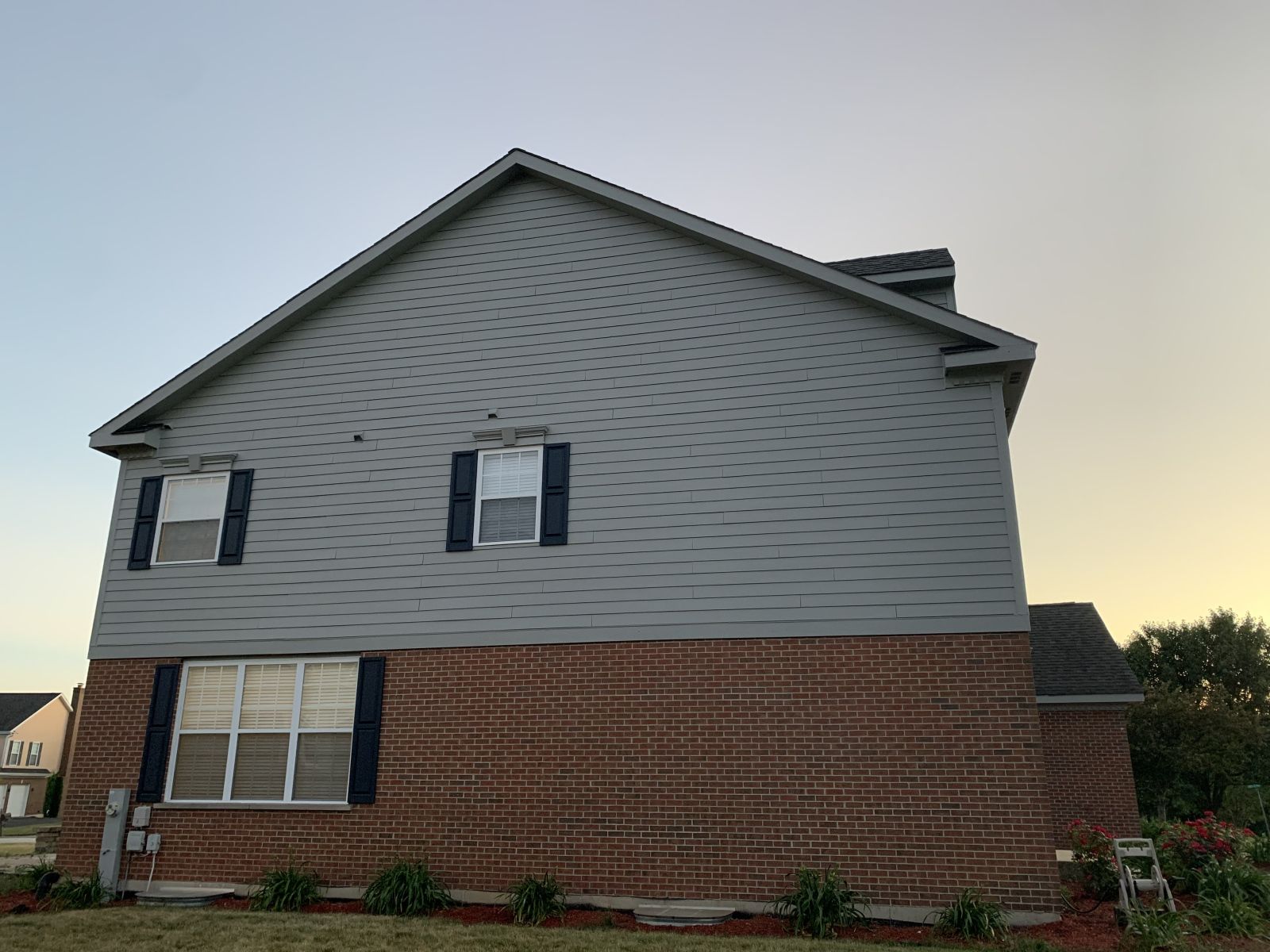 Two-story house with gray siding and red brick exterior at sunset