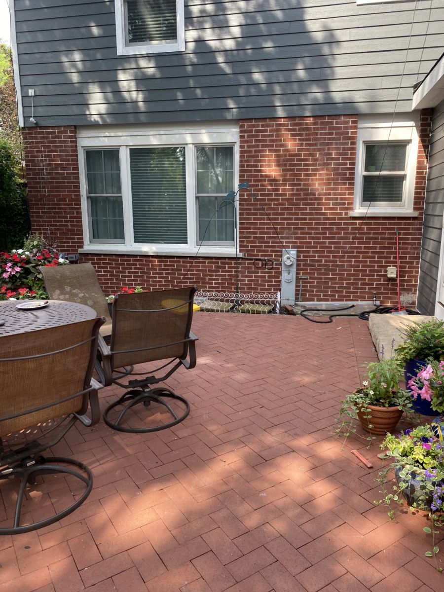 Brick patio with outdoor chairs and potted flowers beside a house exterior and window.