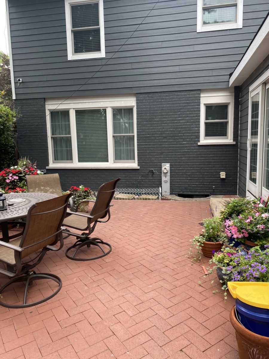 Back patio with brick pavers, patio chairs, flower pots, and gray house siding.