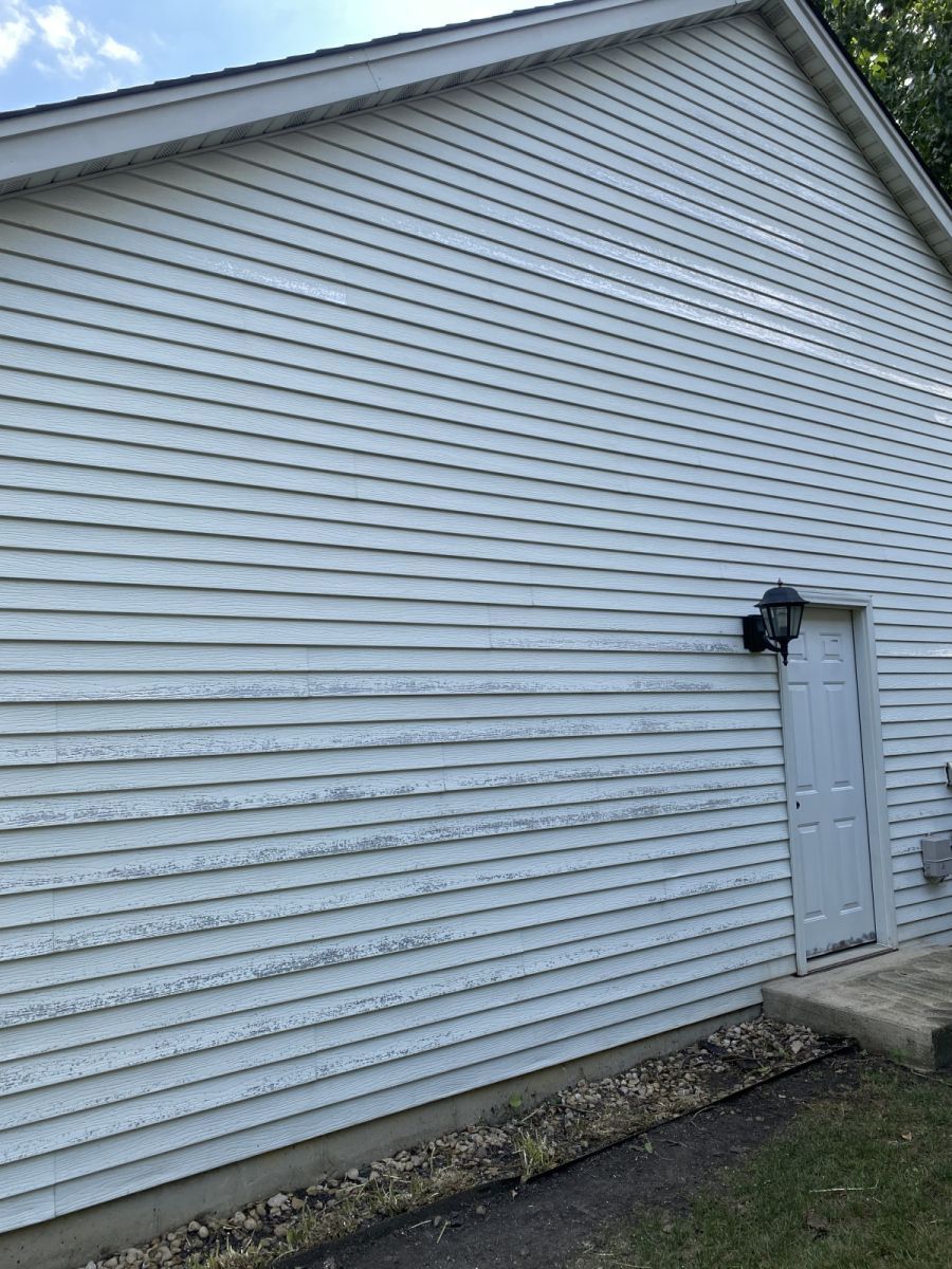White-sided house exterior with a small door and mounted utility fixture near the ground