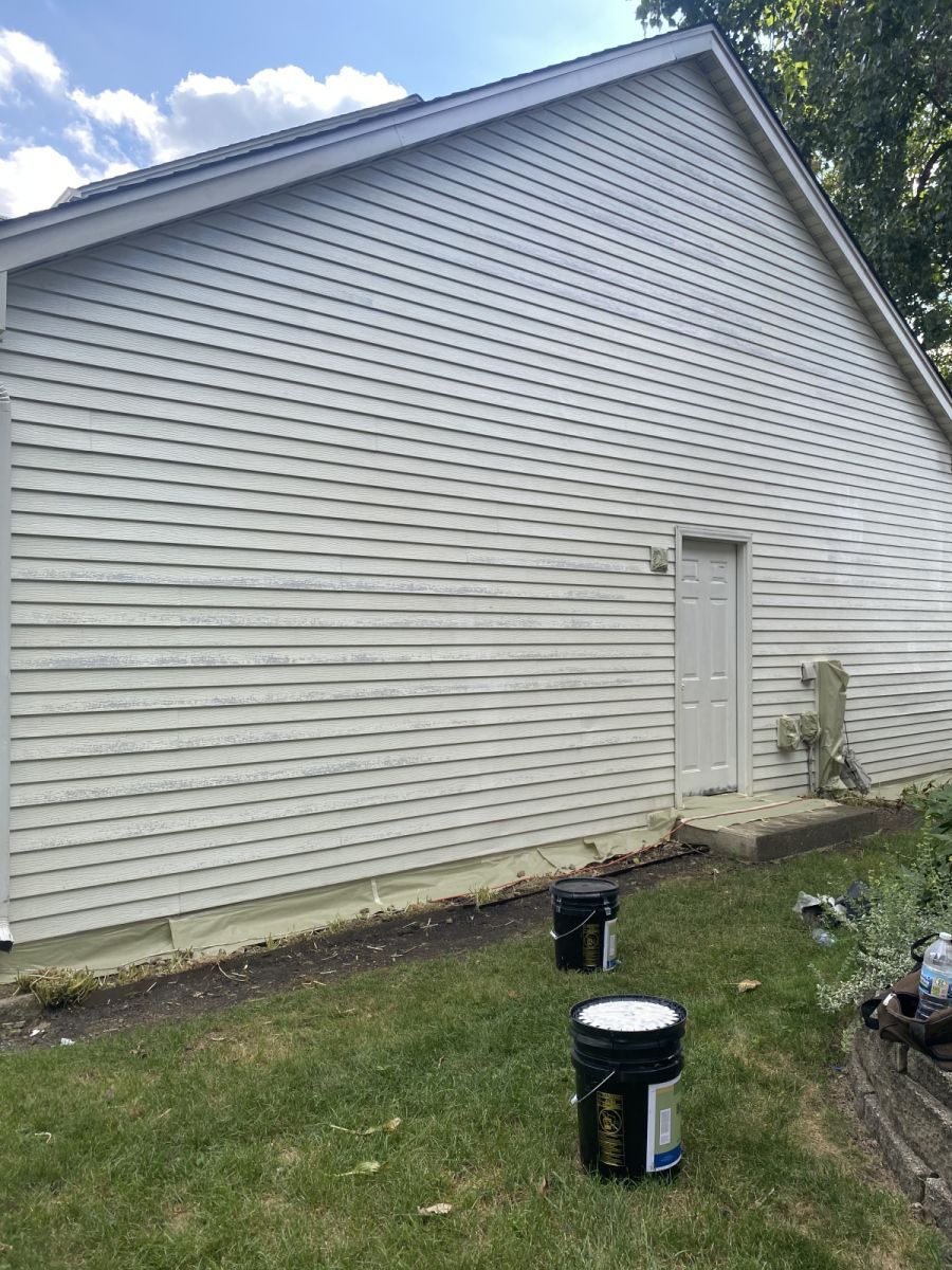 White-sided house exterior with a steep gable roof, small door, and a grassy yard with paint buckets.