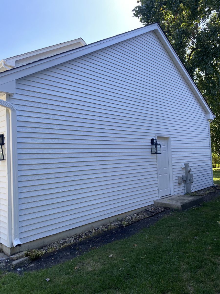 White vinyl-sided house exterior with a side entrance, wall lantern, and grass yard.