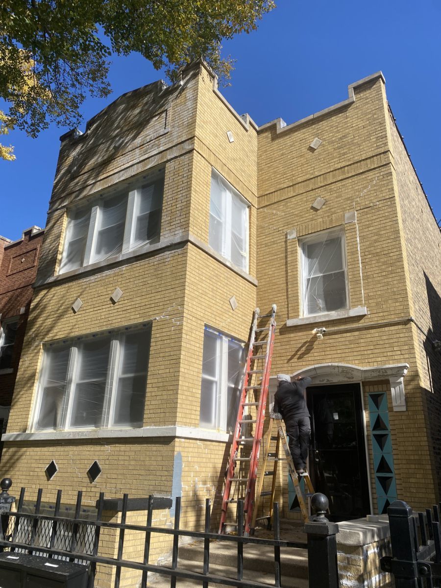 Yellow brick townhouse with a ladder by the front entrance and a black fence in front