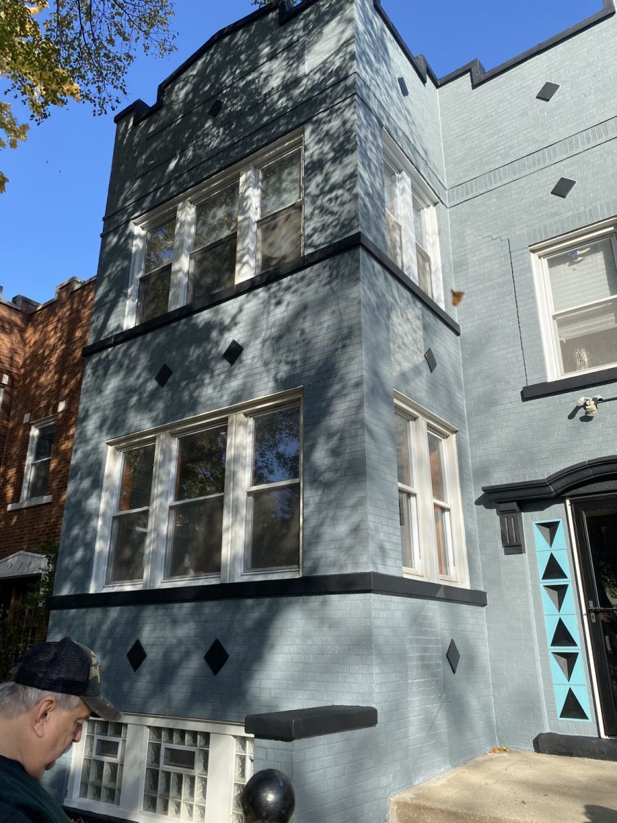 Gray three-story townhouse with white trim and blue door in sunlight, viewed from the street