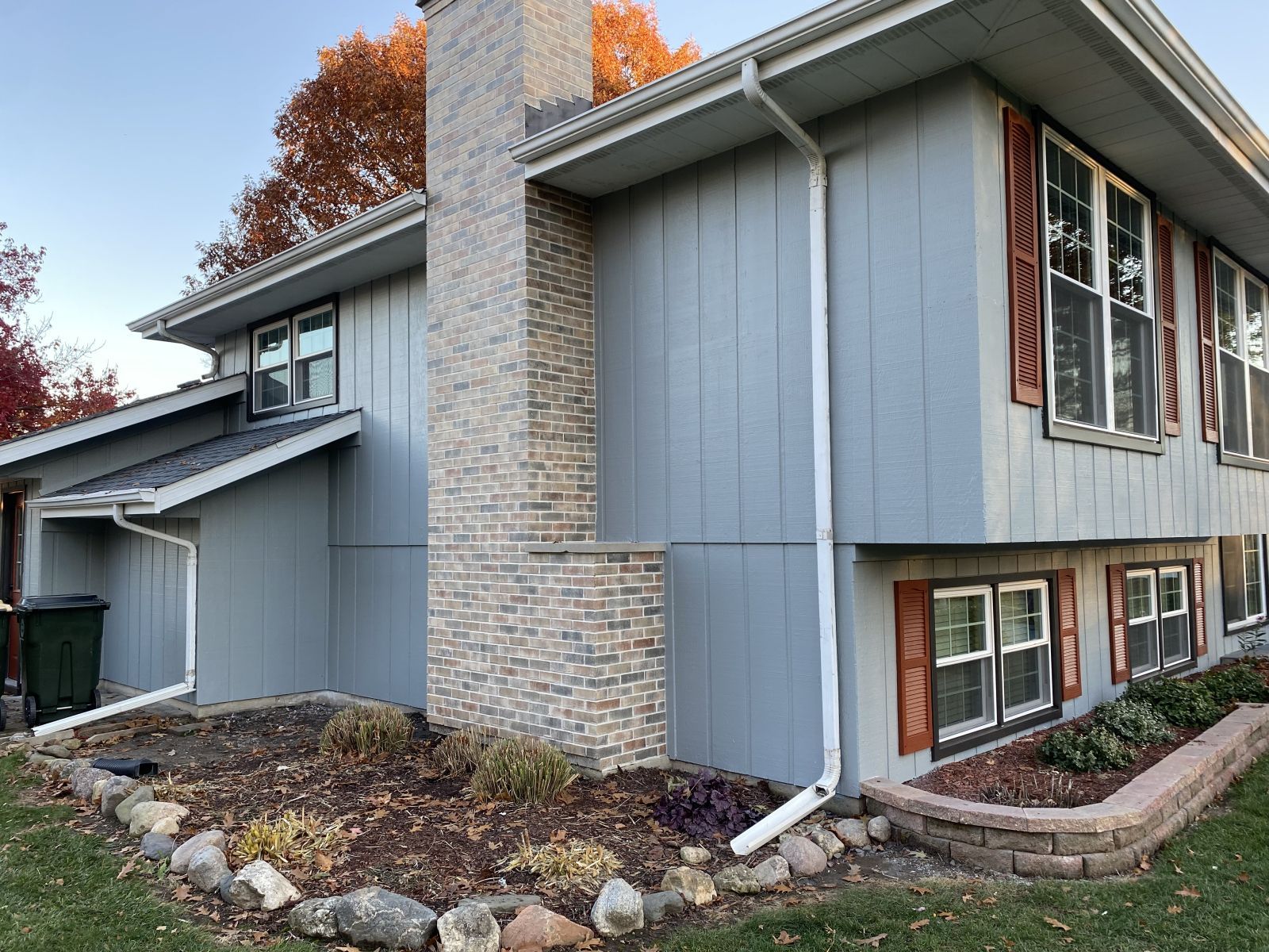 Modern gray house exterior with stone chimney, large windows, and autumn landscaping