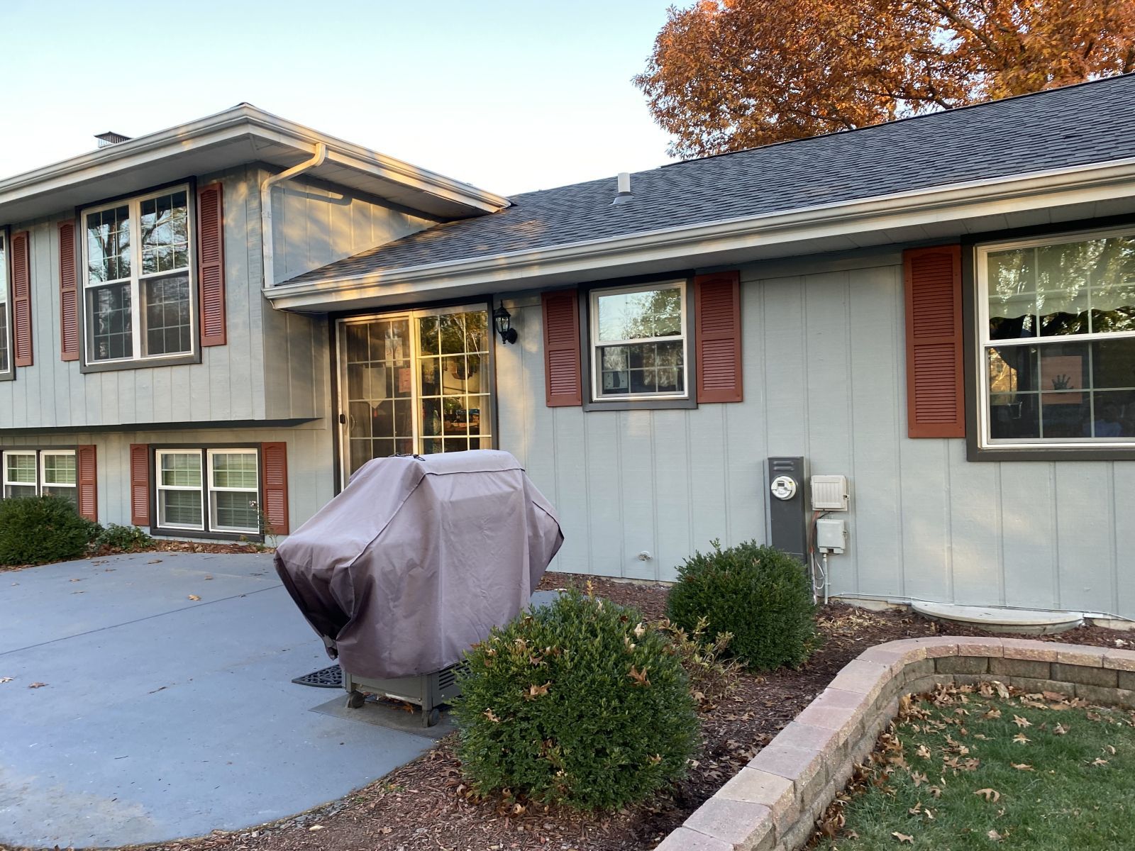 Suburban house exterior with gray siding, two-story section, and a covered grill on the front patio.