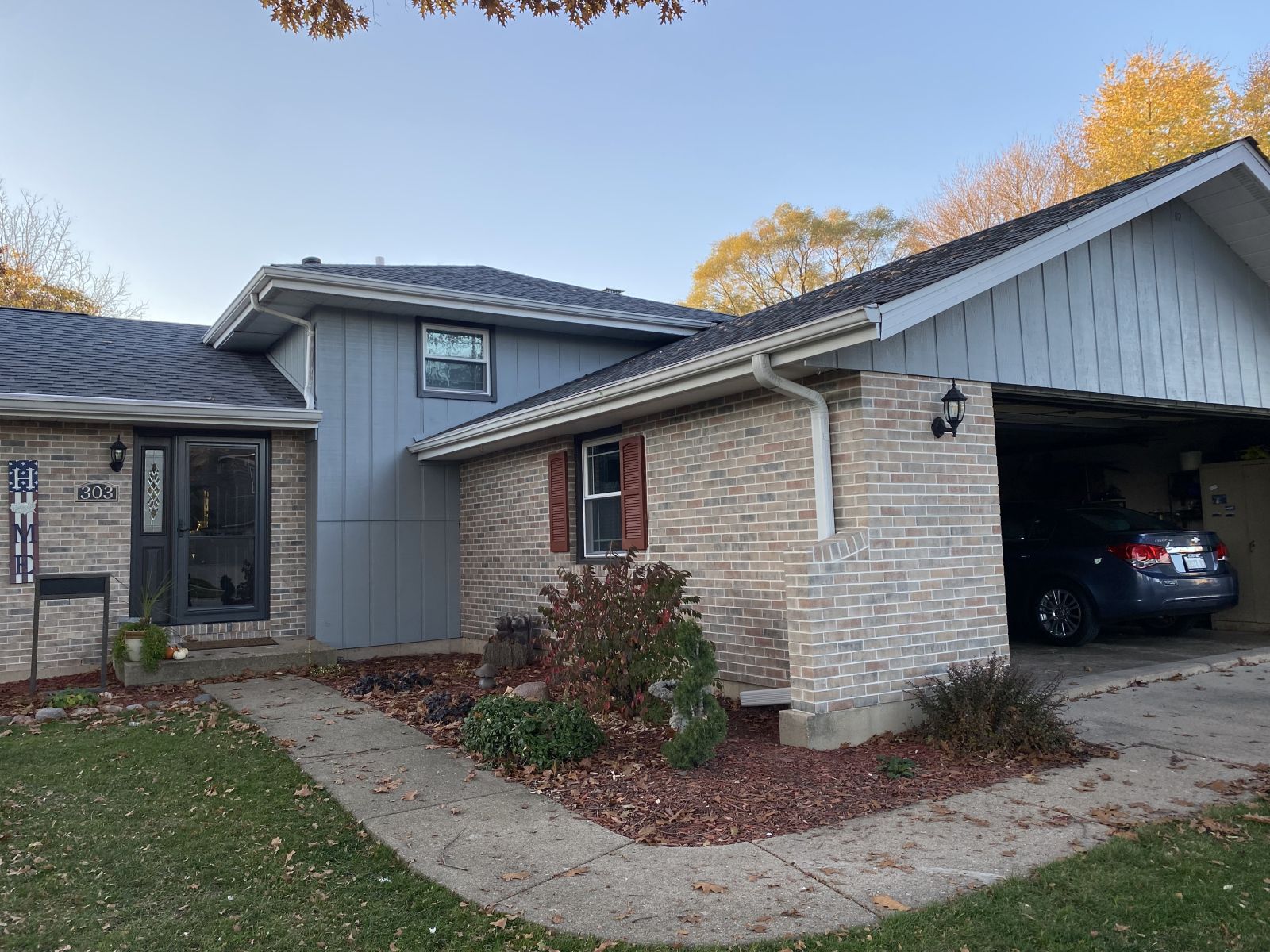 Suburban house exterior with brick and gray siding, open garage, and a car inside.
