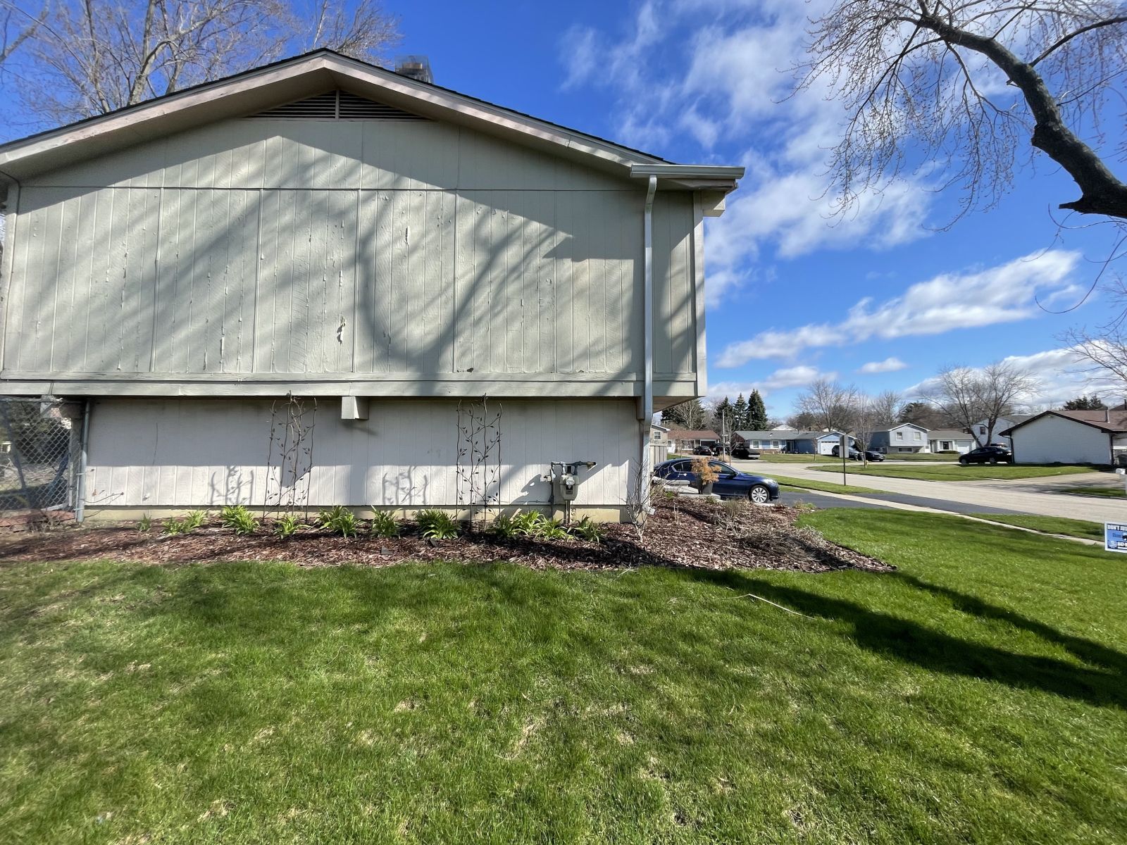 Suburban house exterior with beige siding, green lawn, and blue sky
