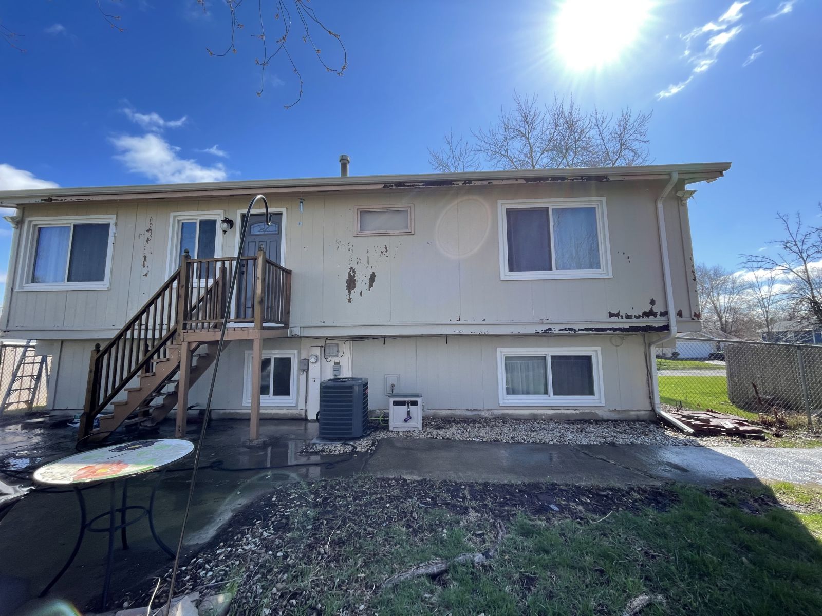 Back of a beige house with a wooden staircase and patio under a bright blue sky