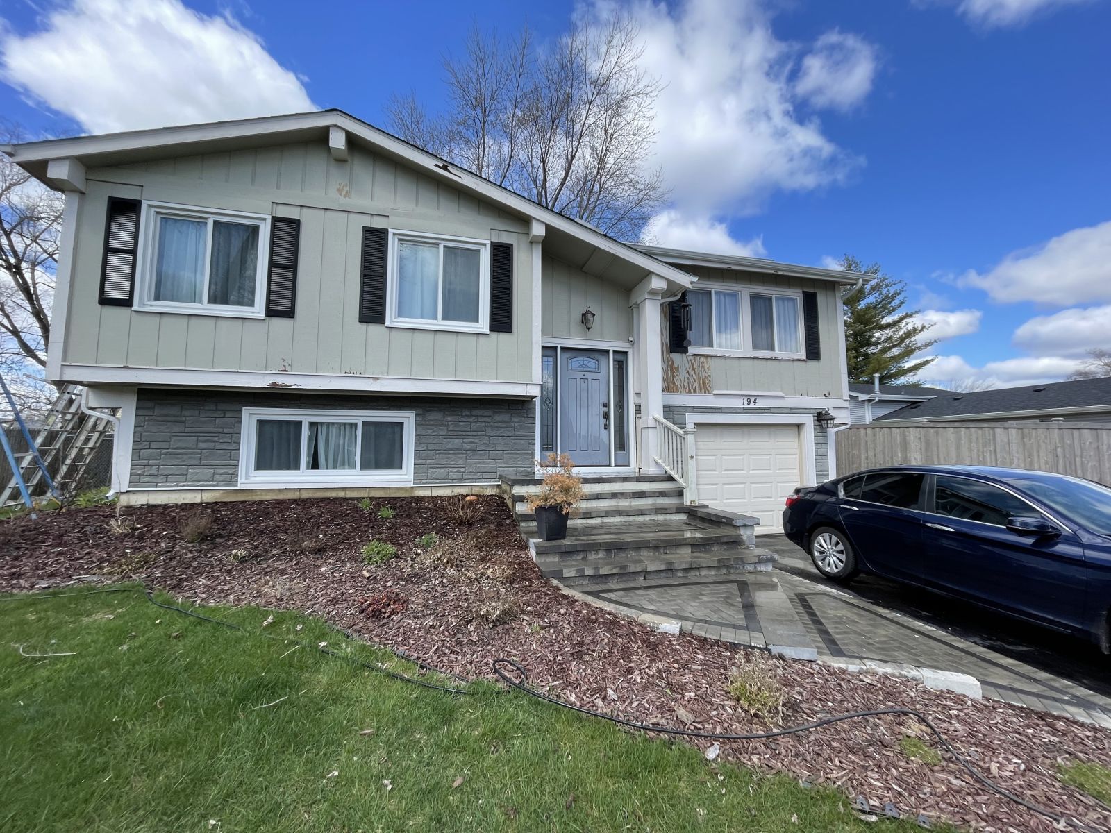 Suburban house with stone steps, garage, and a black car parked in the driveway under a blue sky