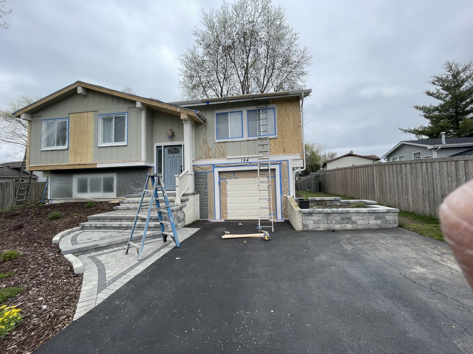 House exterior with a wide driveway, front steps, and garage under a cloudy sky