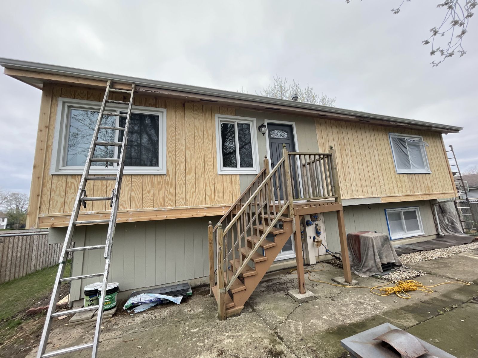 House under renovation with exposed insulation, front stairs, and a ladder leaning against the upper level