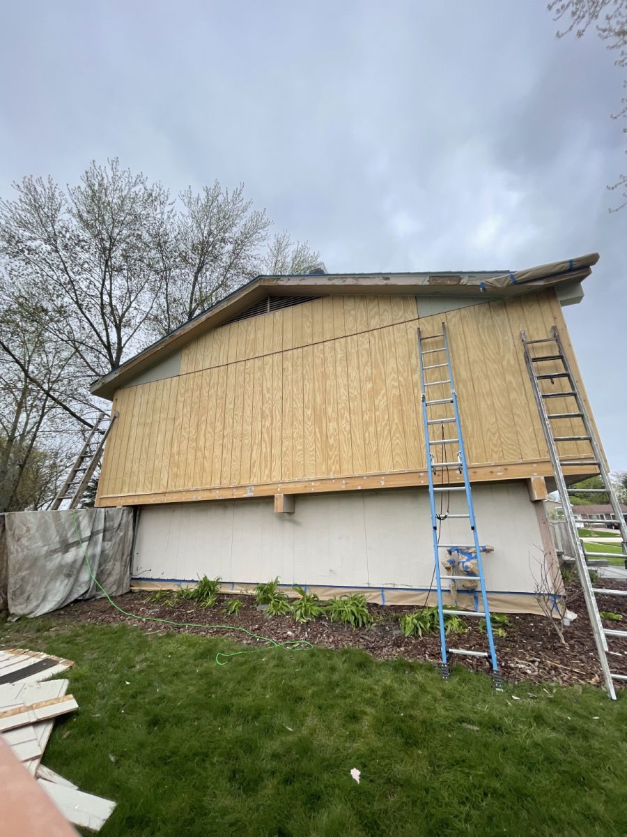 House exterior under construction with bamboo-like siding, ladder, and overcast sky