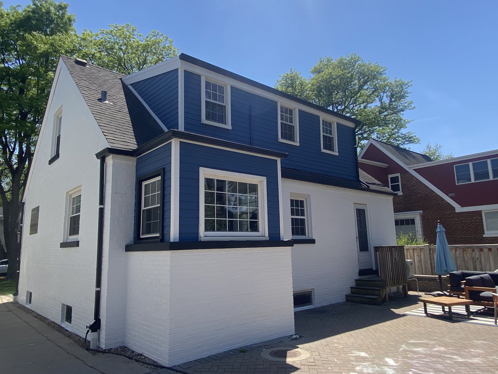 White house with blue upper siding and black-trimmed windows, seen from the side on a sunny day.