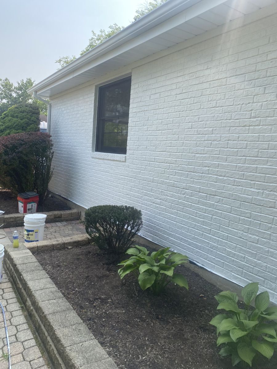 White brick house exterior with a window, shrubs, and a concrete walkway along the side yard